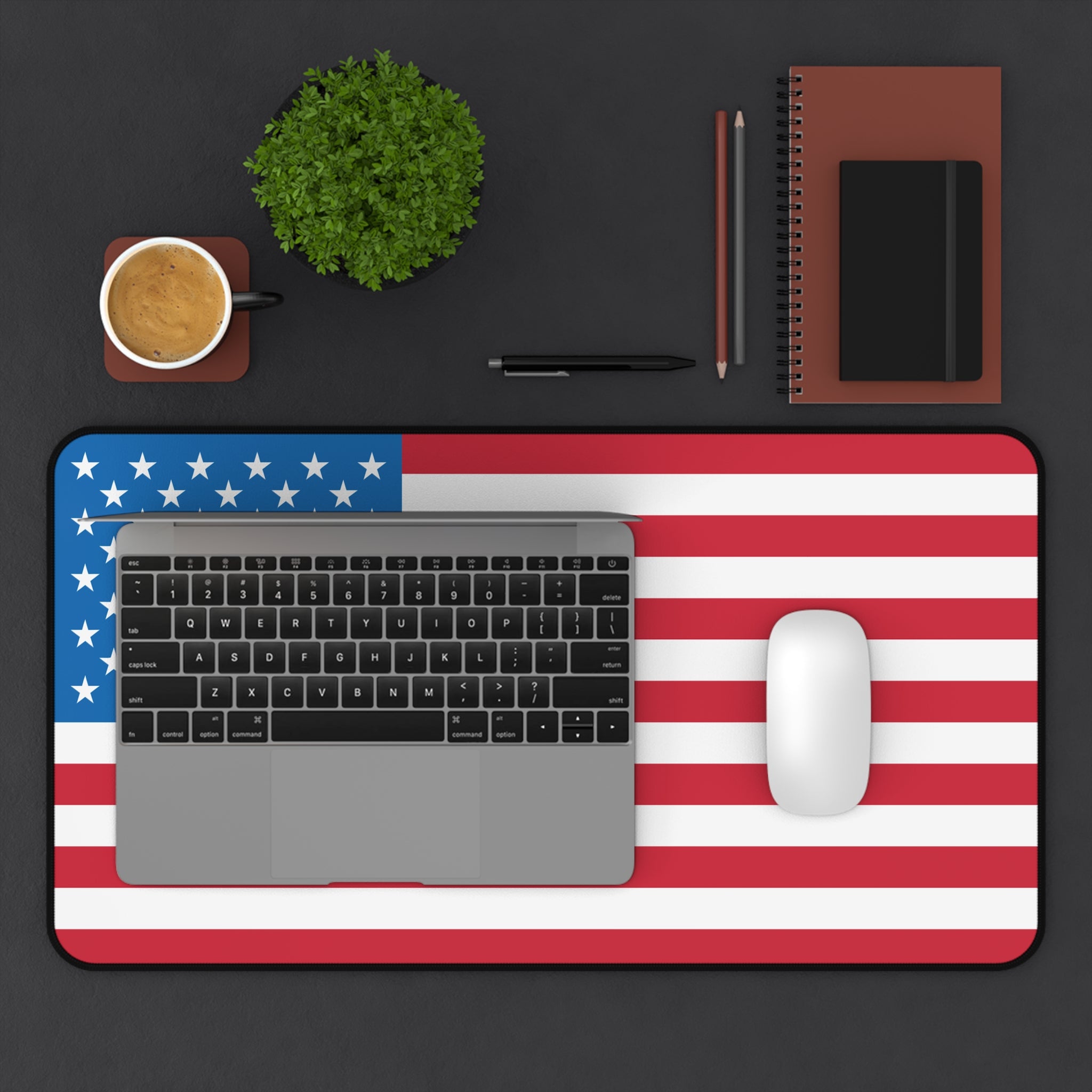 Laptop on an American flag desk mat with a cup, plant, and office supplies on a black background