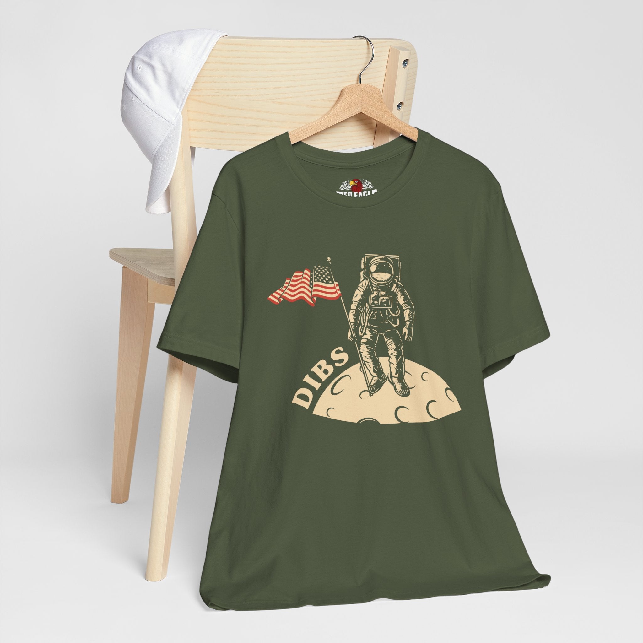 Military Green t-shirt with astronaut graphic and 'DIBS' text on a wooden chair.