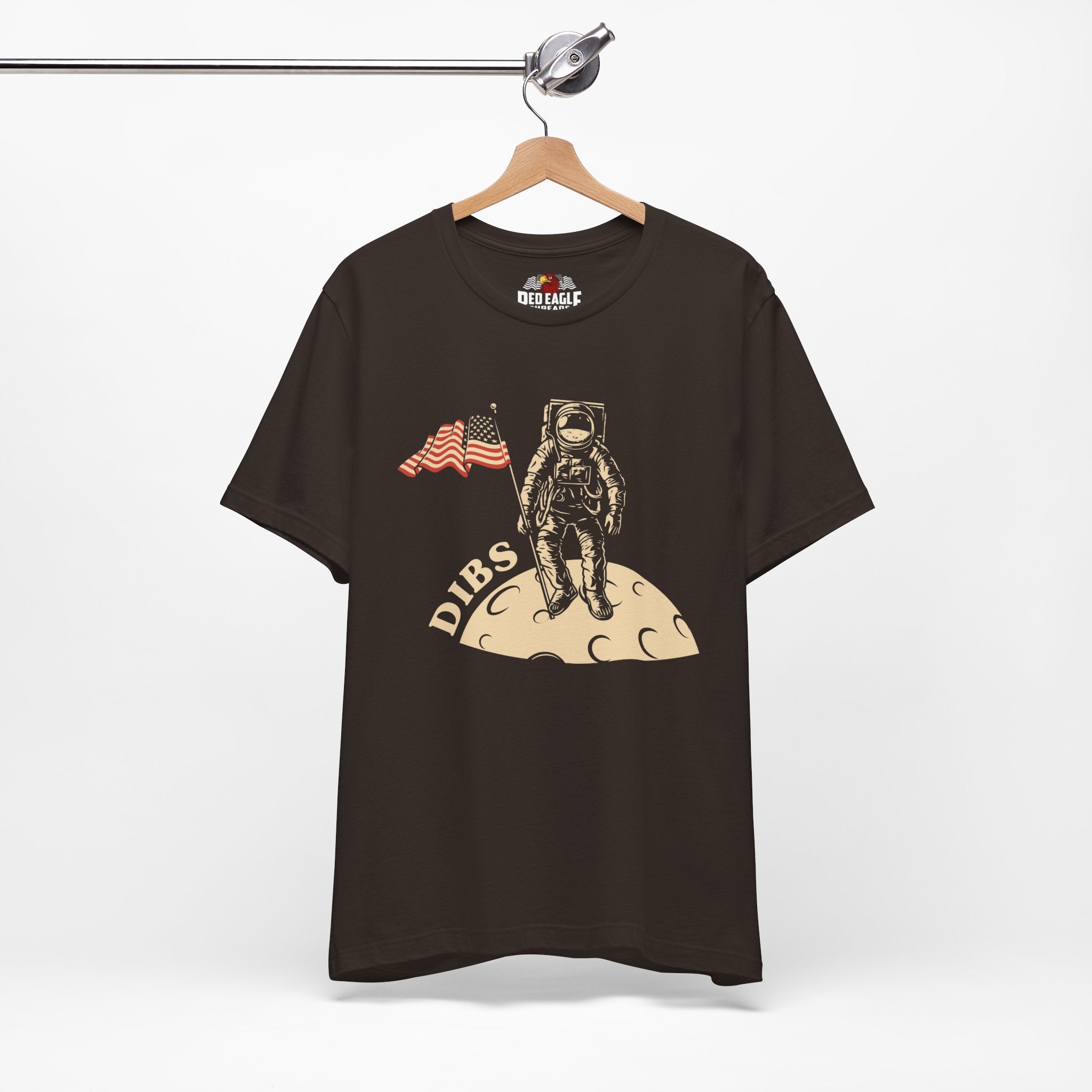 Brown t-shirt with astronaut graphic and 'DIBS' text on a hanger against a white background