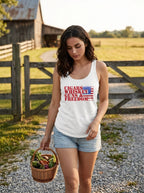A woman standing outdoors on a gravel path near a wooden fence and barn, wearing a white tank top with a red and blue graphic that reads 'CIGARS WHISKEY GUNS & FREEDOM' and denim shorts, while holding a basket of vegetables. (AI generated)