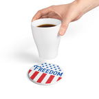 Hand holding a white mug with a 'Freedom' coaster underneath on a white background