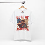 White t-shirt with graphic design of a person holding a gun and 'Gulf of America' text, hanging on a wooden hanger.