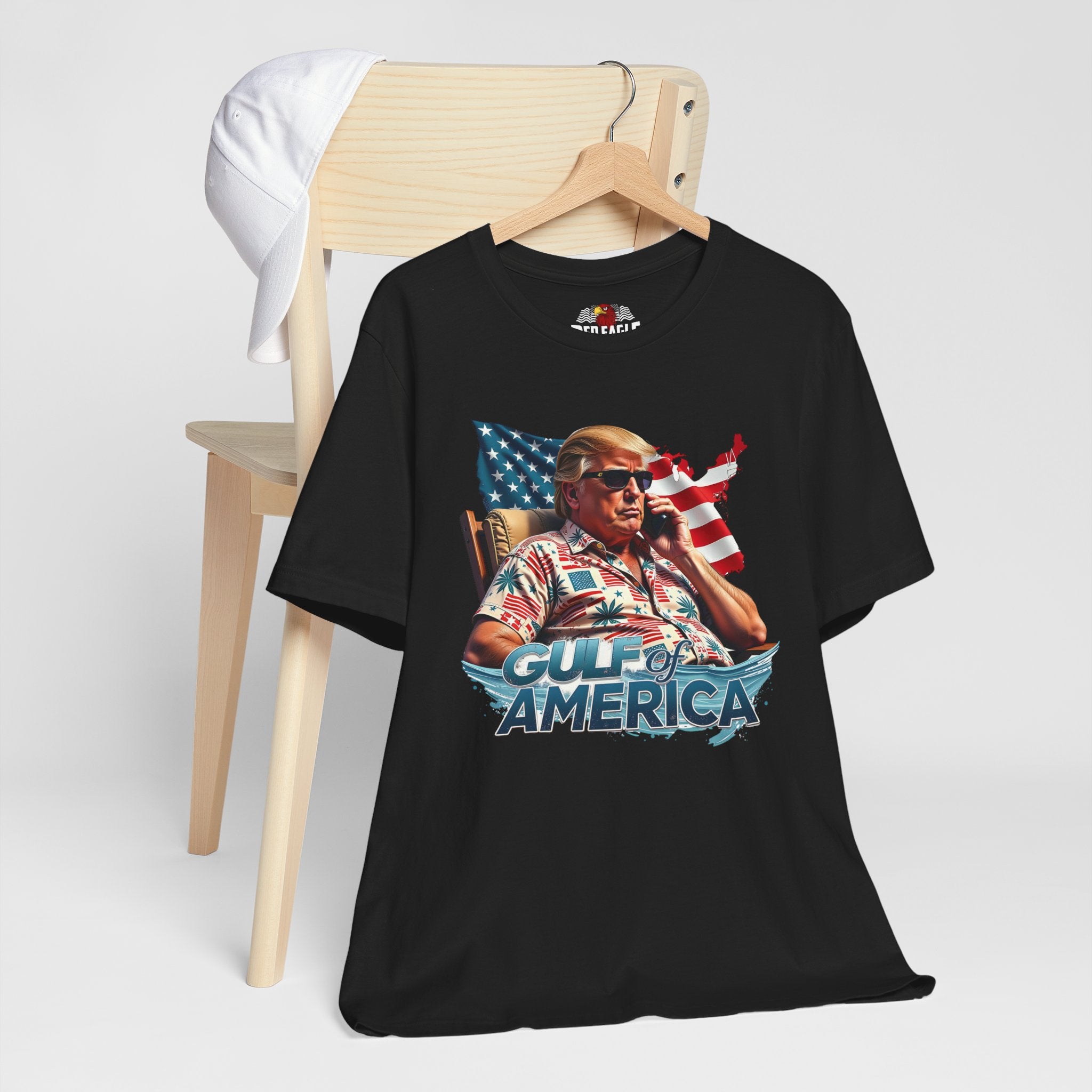 Black t-shirt with graphic design of a person holding a phone in front of an American flag, sitting in a chair, with 'Gulf of America' text on a white background.