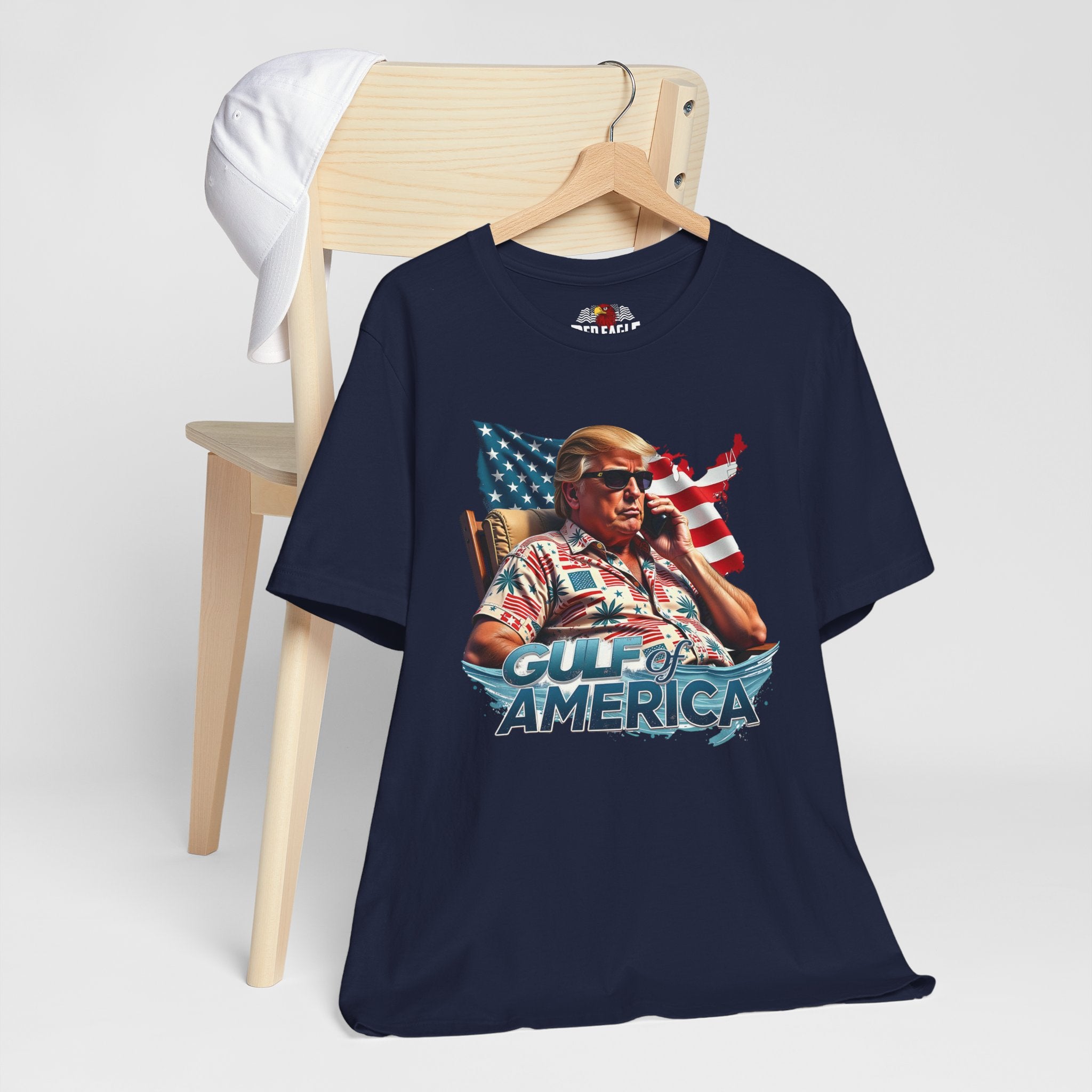 Navy blue t-shirt with graphic design of a person holding a phone in front of an American flag, sitting in a chair, with 'Gulf of America' text on a white background.