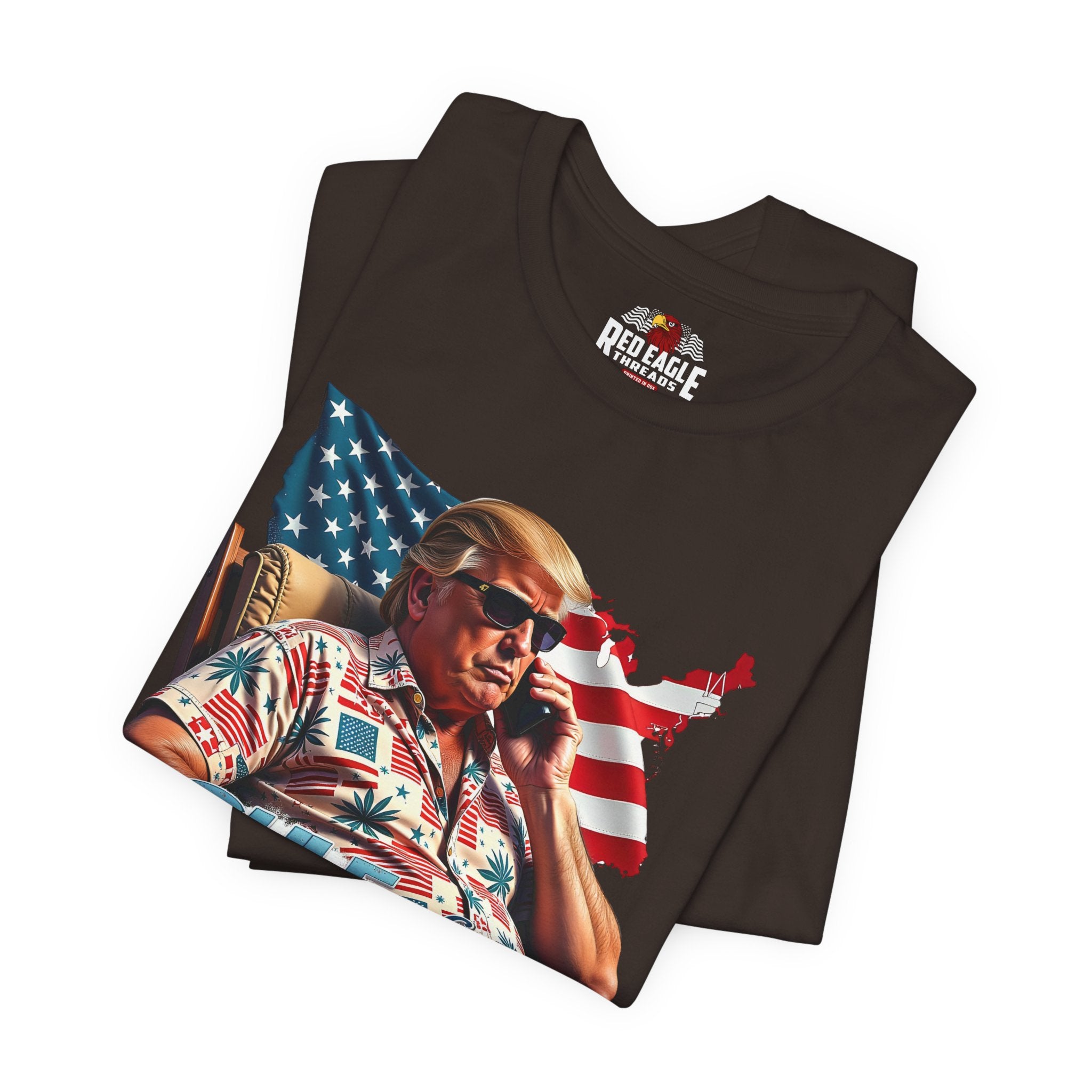 Folded brown t-shirt with a graphic of a person holding a phone in front of an American flag.