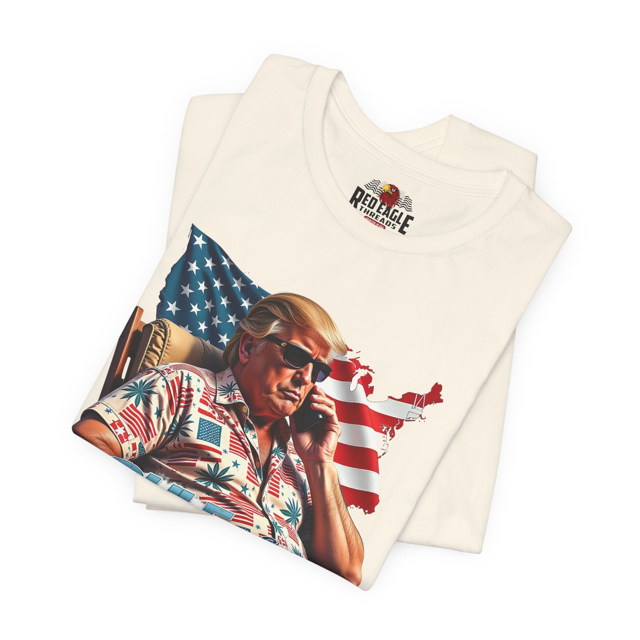 Folded natural t-shirt with a graphic of a person holding a phone in front of an American flag.