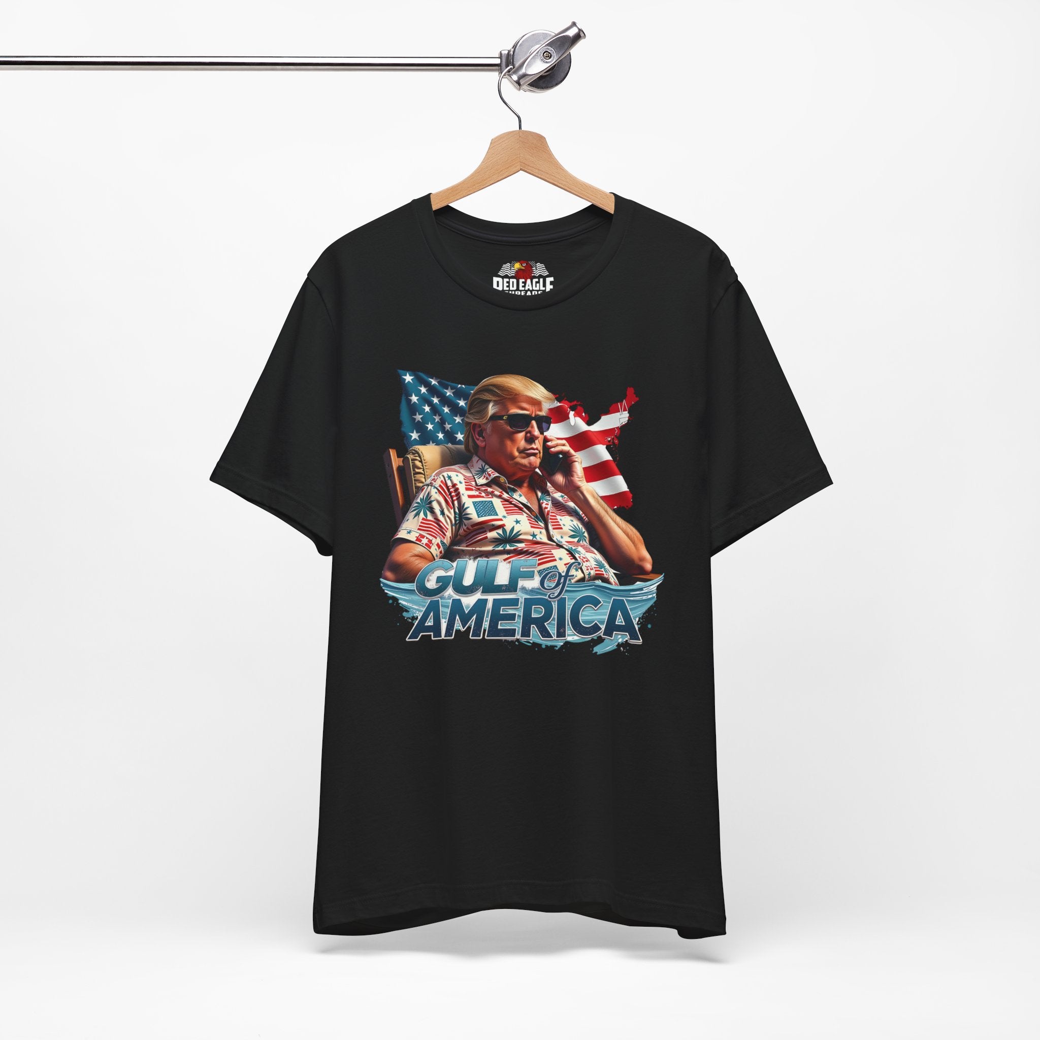 Black t-shirt with graphic design of a person holding an American flag, labeled 'Gulf of America', on a hanger against a white background.