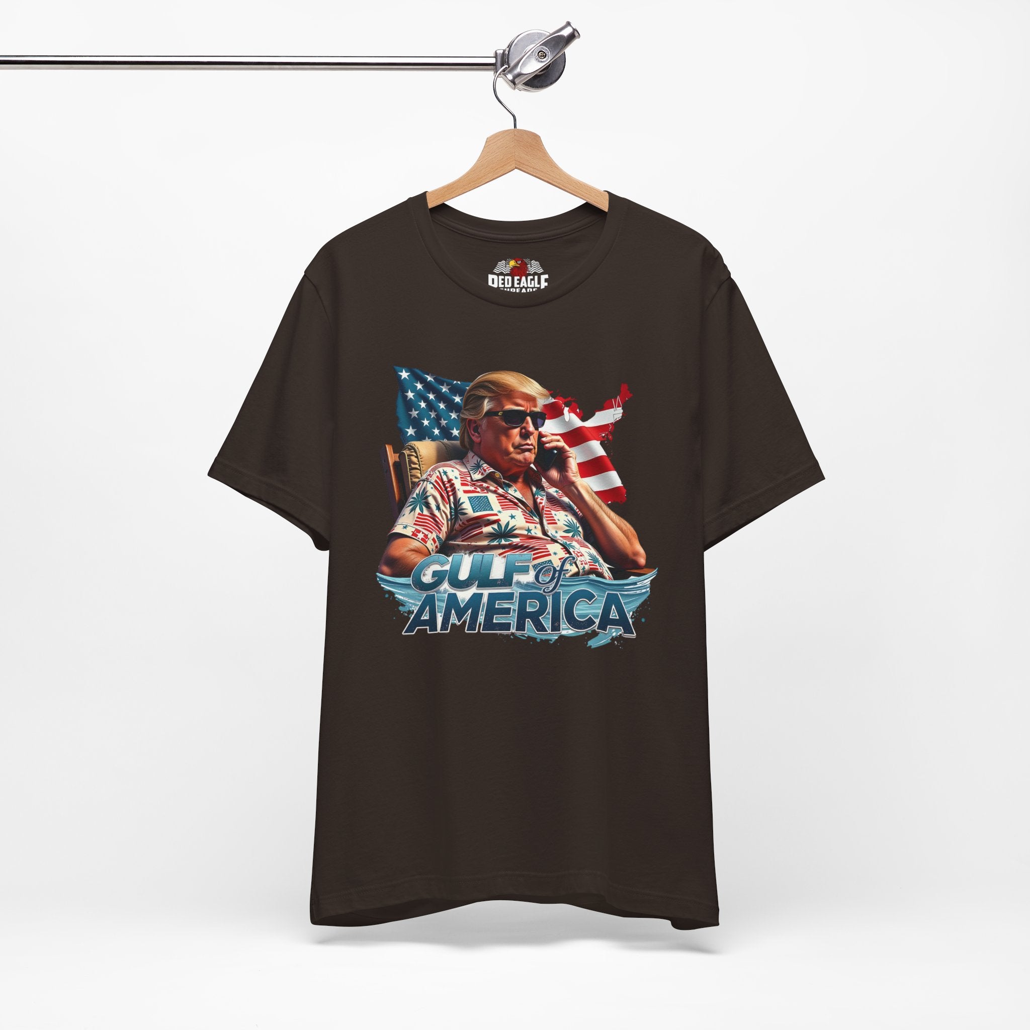 Brown t-shirt with graphic design of a person holding an American flag, labeled 'Gulf of America', on a hanger against a white background.