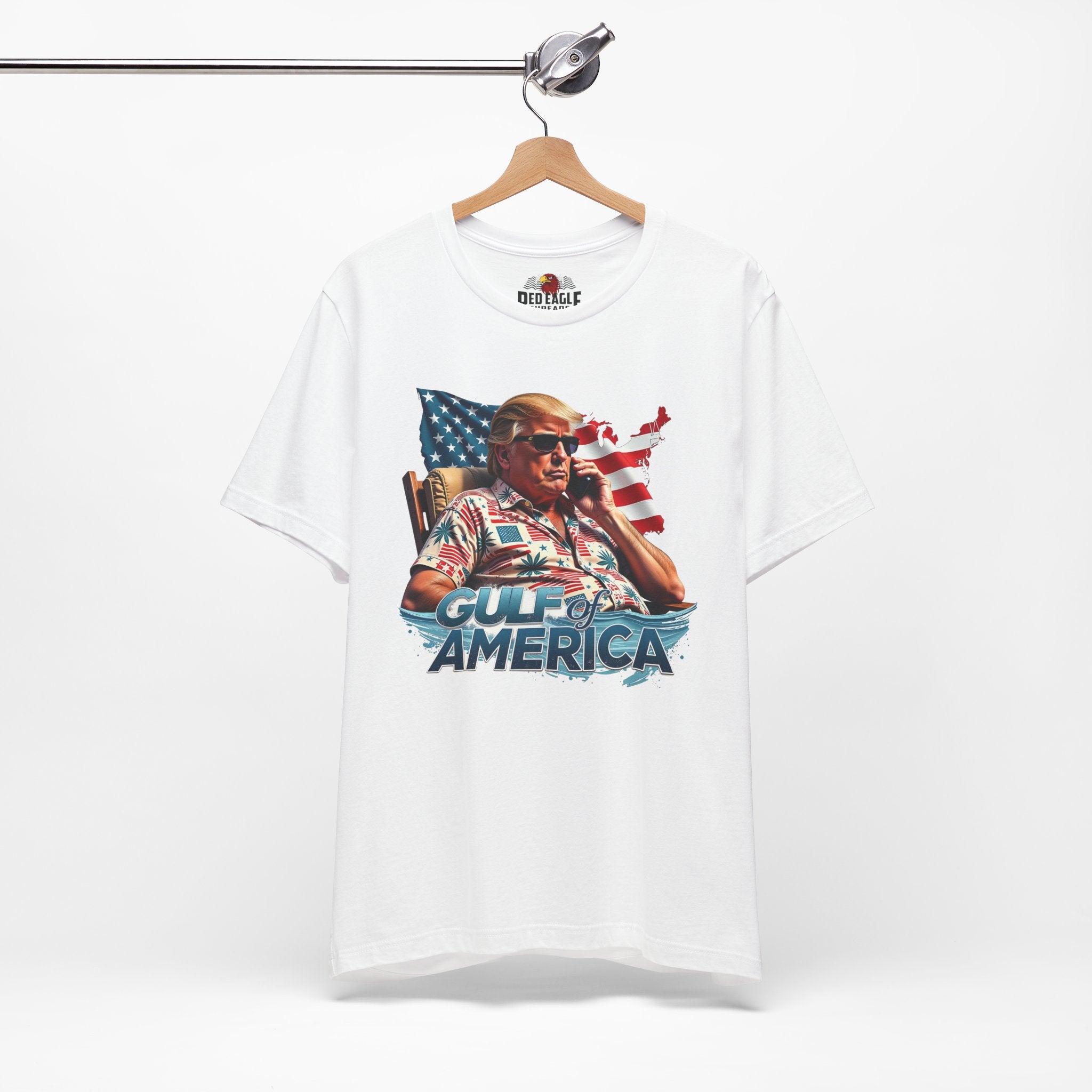 White t-shirt with graphic design of a person holding an American flag, text 'Gulf of America', and a brand logo on a white background.