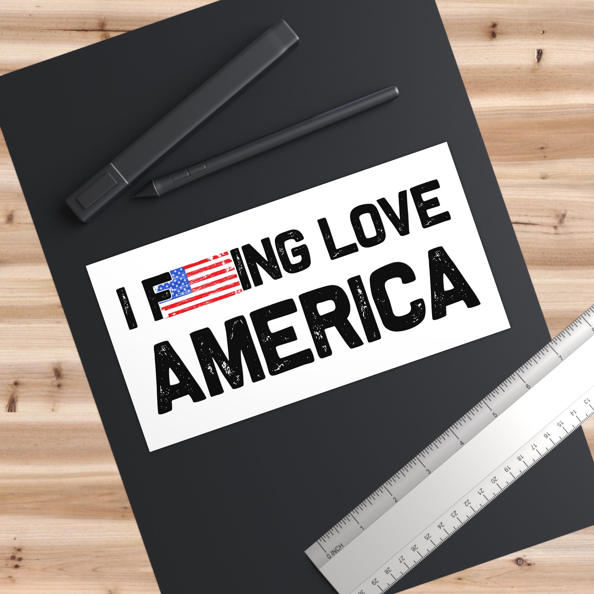 Black folder with 'I F***ING LOVE AMERICA' text and American flag on a wooden surface with pens and a ruler.