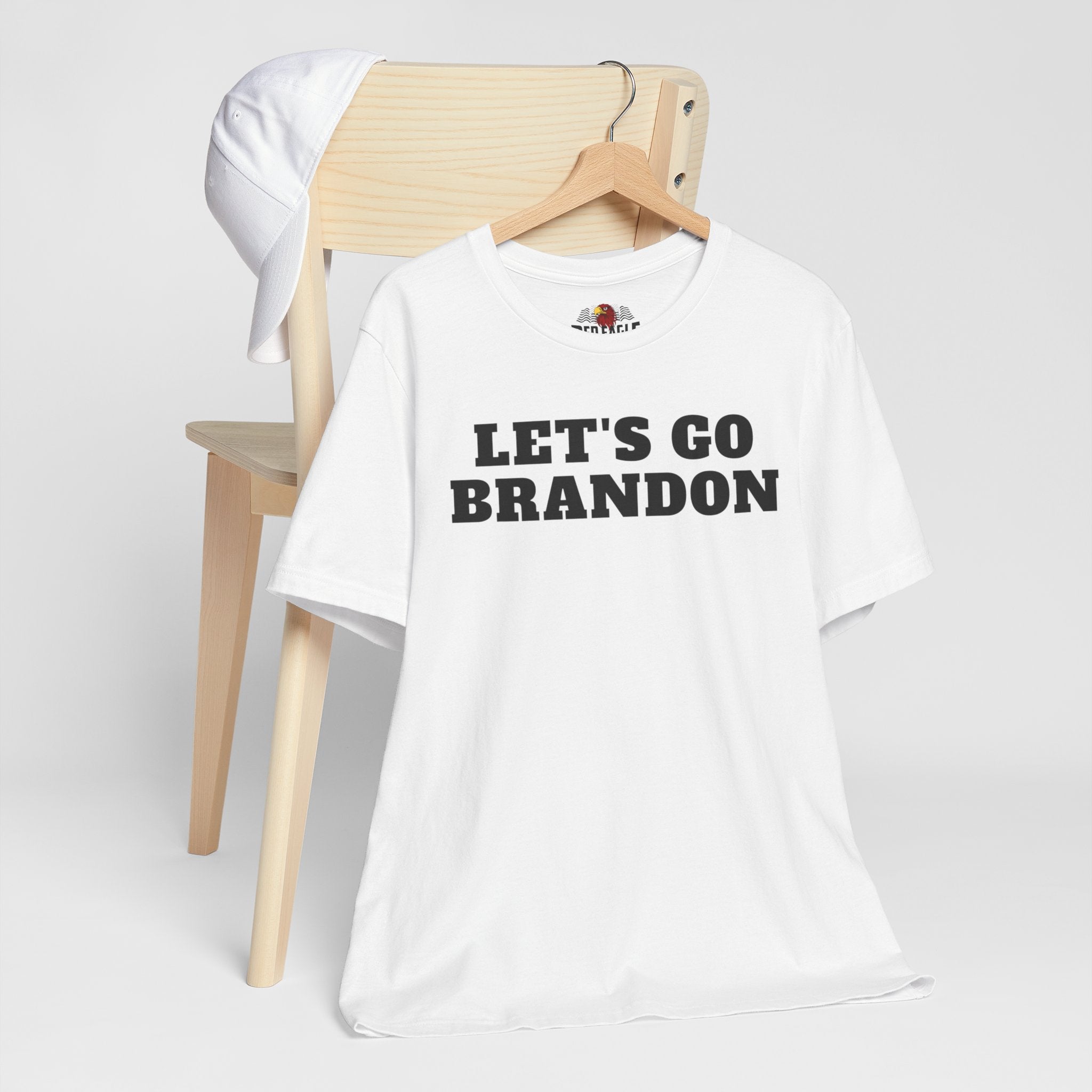 White t-shirt with 'LET'S GO BRANDON' text on a wooden chair against a white background