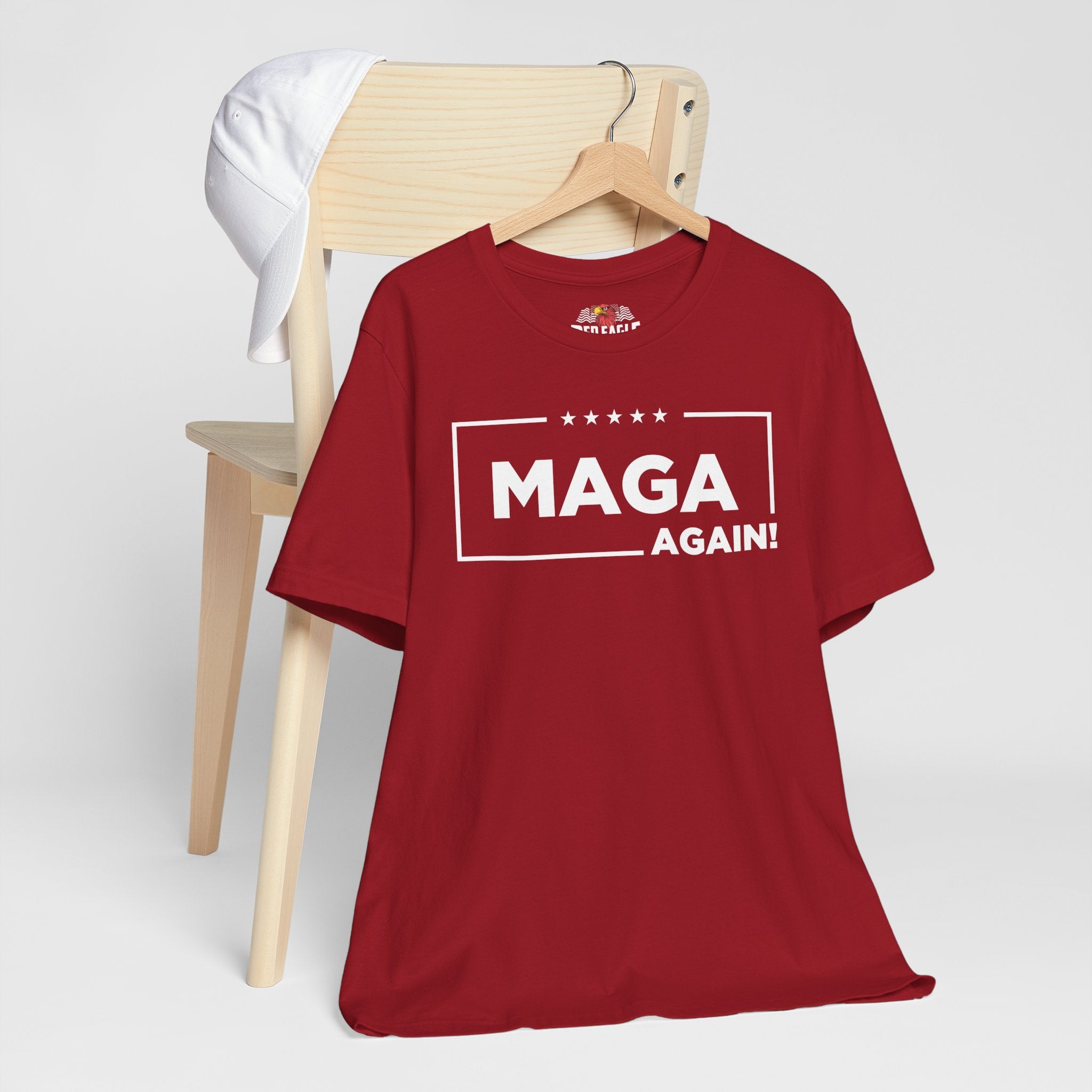 Red t-shirt with 'MAGA AGAIN!' text on a wooden chair against a white background
