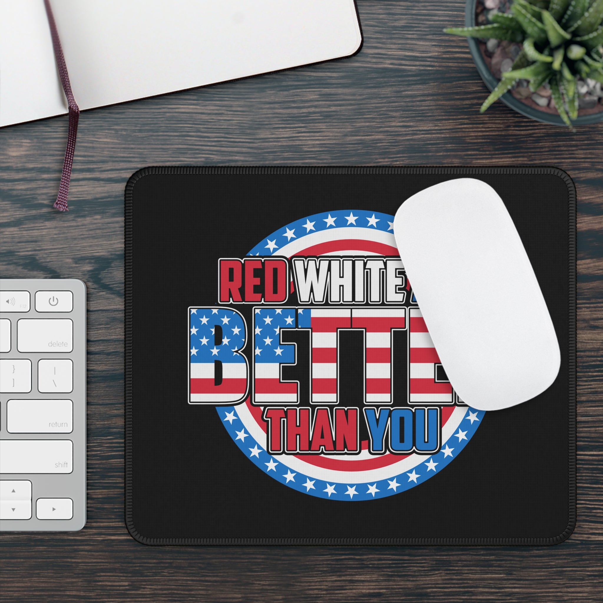 Mouse pad with American flag design and text on a desk with a keyboard and plant.