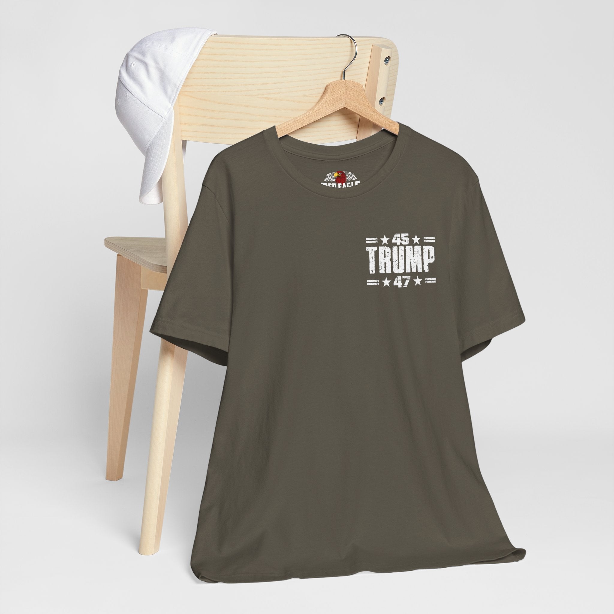 Army green t-shirt with '45 Trump 47' text on a wooden chair against a white background
