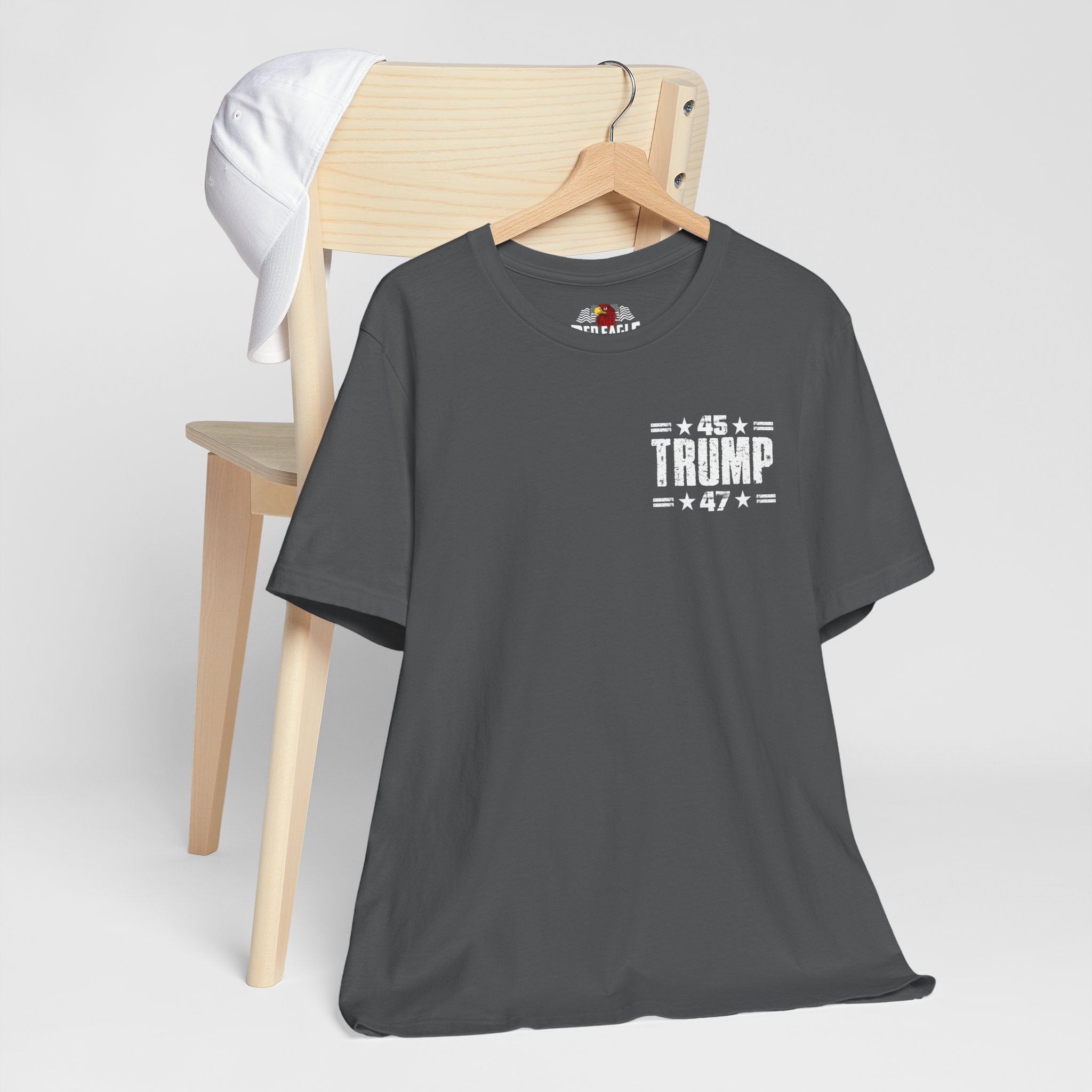 Gray t-shirt with '45 Trump 47' text on a wooden chair against a white background