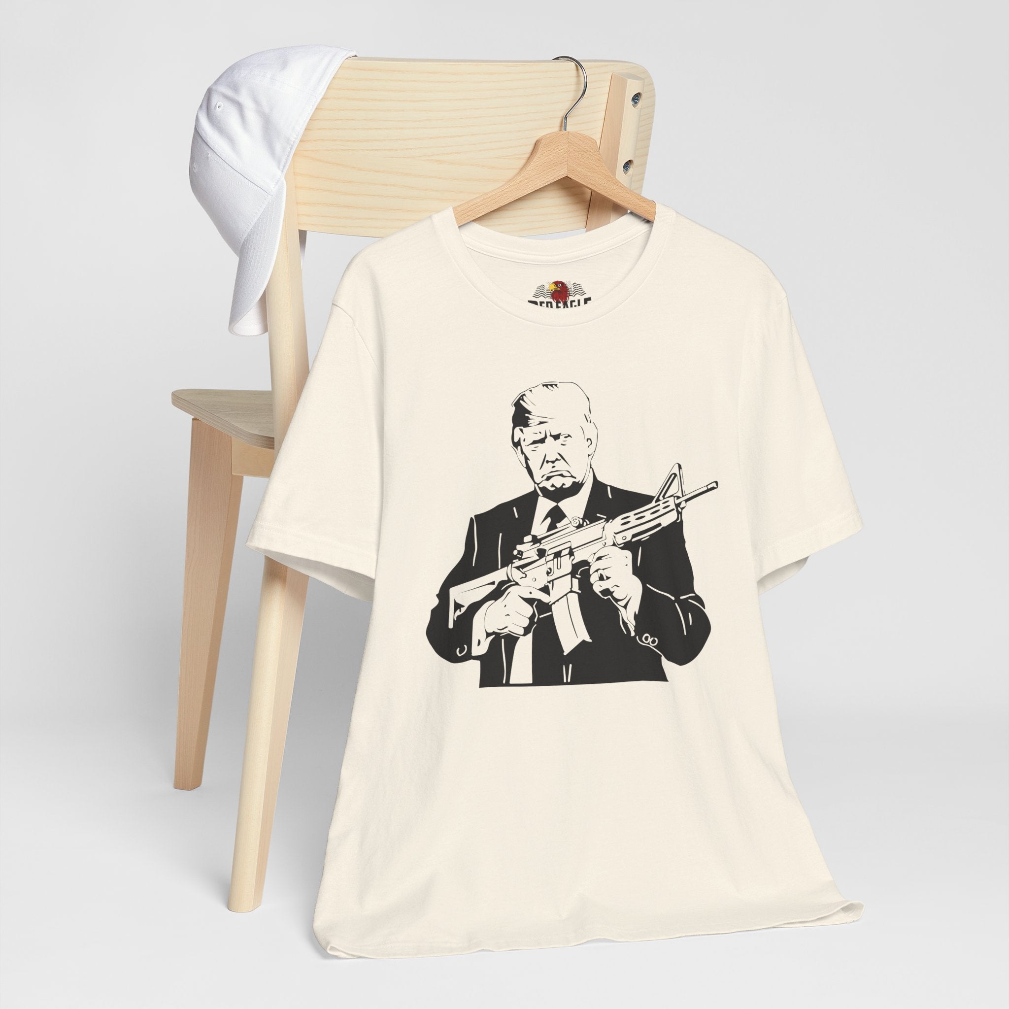 Natural t-shirt with graphic design of a person holding a rifle, displayed on a wooden chair.
