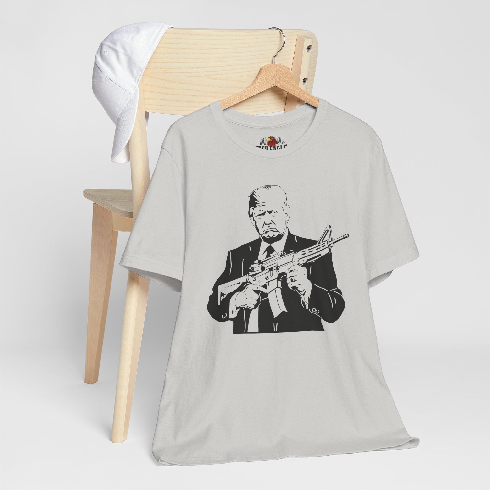 Silver t-shirt with a graphic design of a person holding a rifle, displayed on a wooden chair.