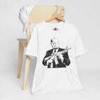 White t-shirt with graphic design of a person holding a rifle, displayed on a wooden chair.