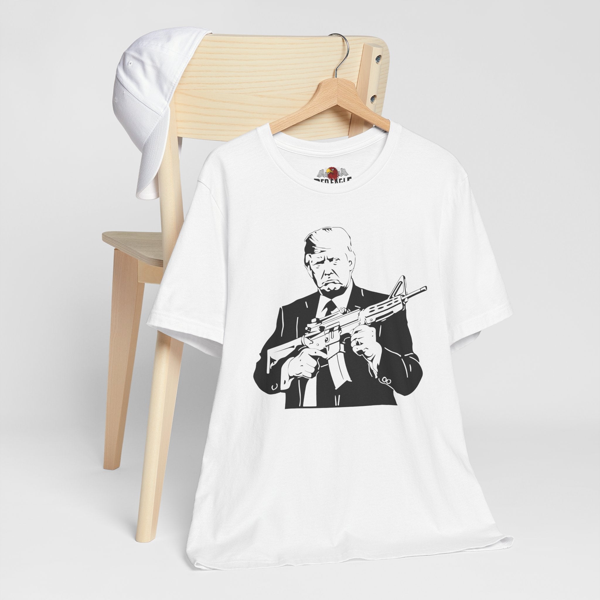 White t-shirt with graphic design of a person holding a rifle, displayed on a wooden chair.