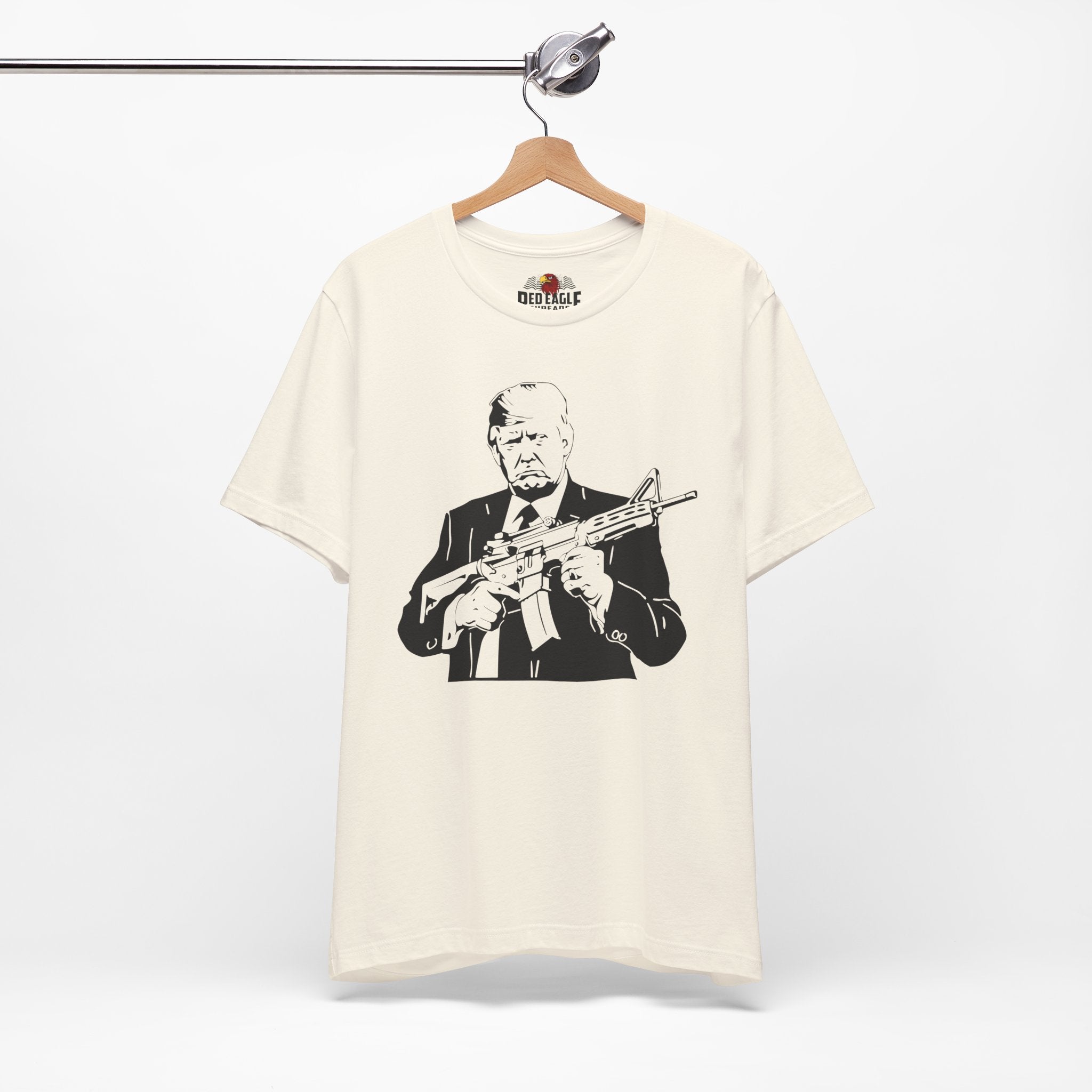 Natural t-shirt with a graphic of a man holding a rifle on a hanger against a white background.