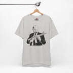 Silver t-shirt with graphic design of a person holding a rifle, hanging on a wooden hanger against a white background.