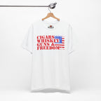 White t-shirt with 'Cigars Whiskey Guns & Freedom' text and American flag design on a hanger.