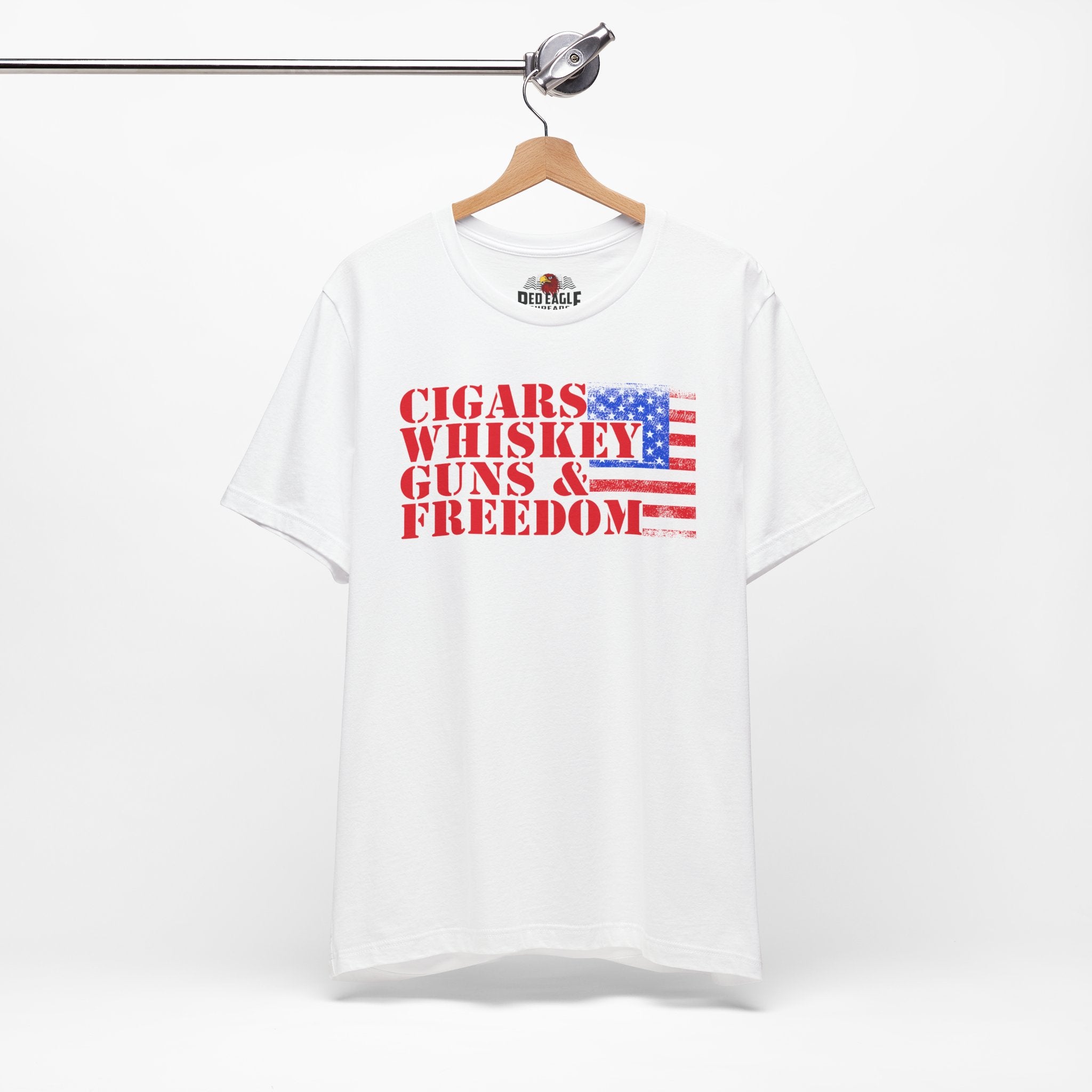 White t-shirt with 'Cigars Whiskey Guns & Freedom' text and American flag design on a hanger.