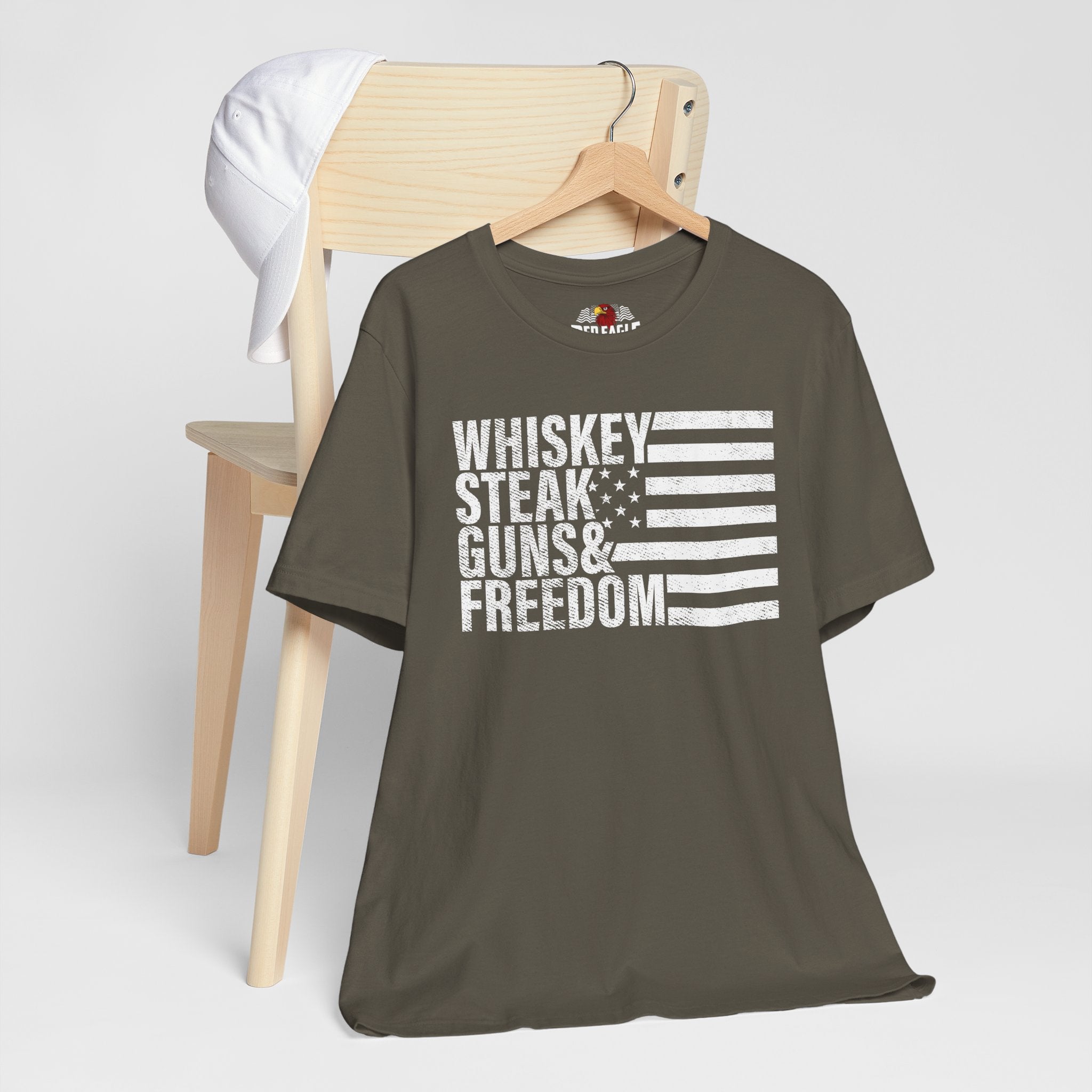 Army t-shirt with 'Whiskey Steak Guns & Freedom' text on a wooden chair against a white background