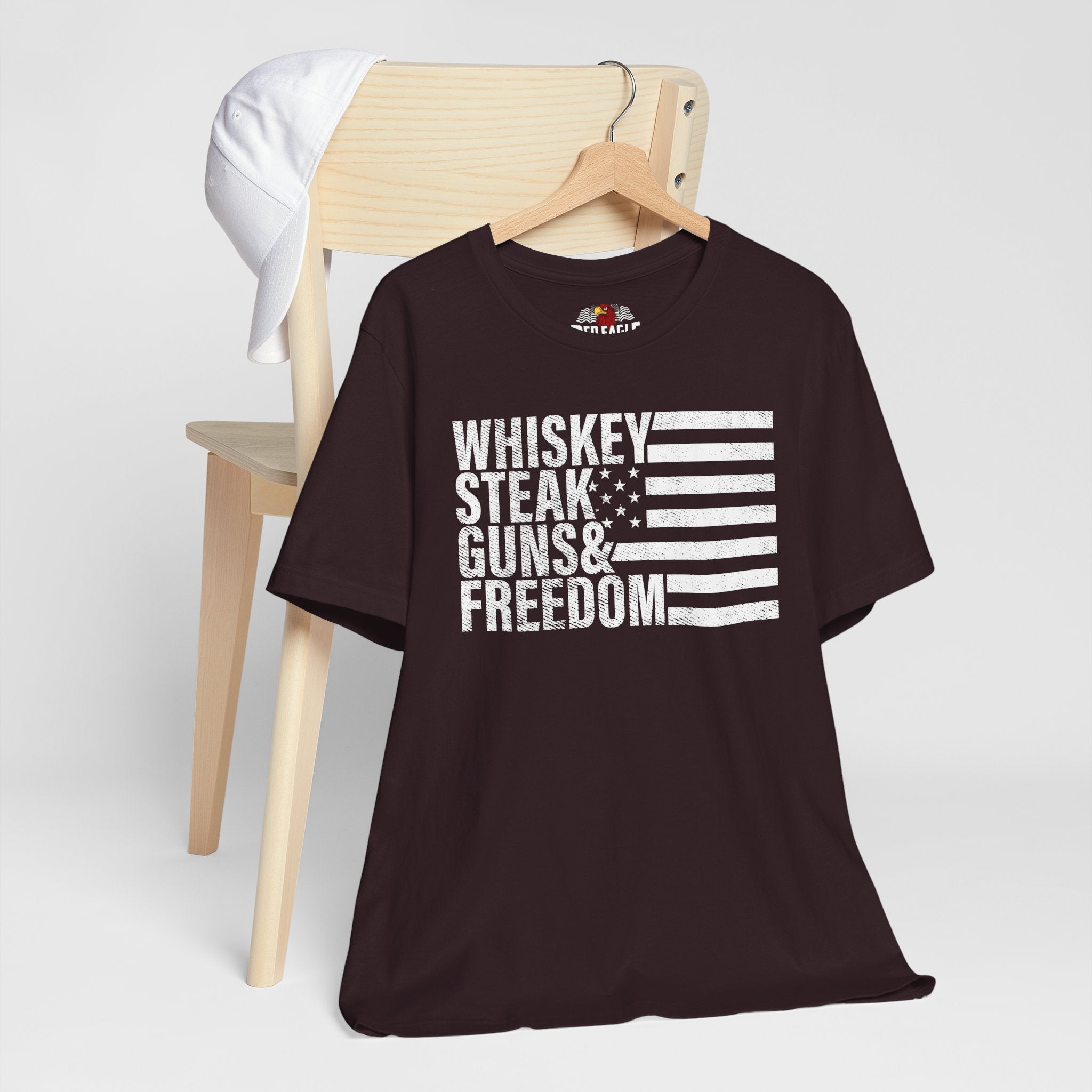 Oxblood Black t-shirt with 'Whiskey Steak Guns & Freedom' text and flag design on a wooden chair.