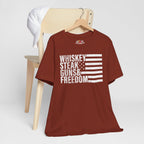 Rust t-shirt with 'Whiskey Steak Guns & Freedom' text on a wooden chair against a white background