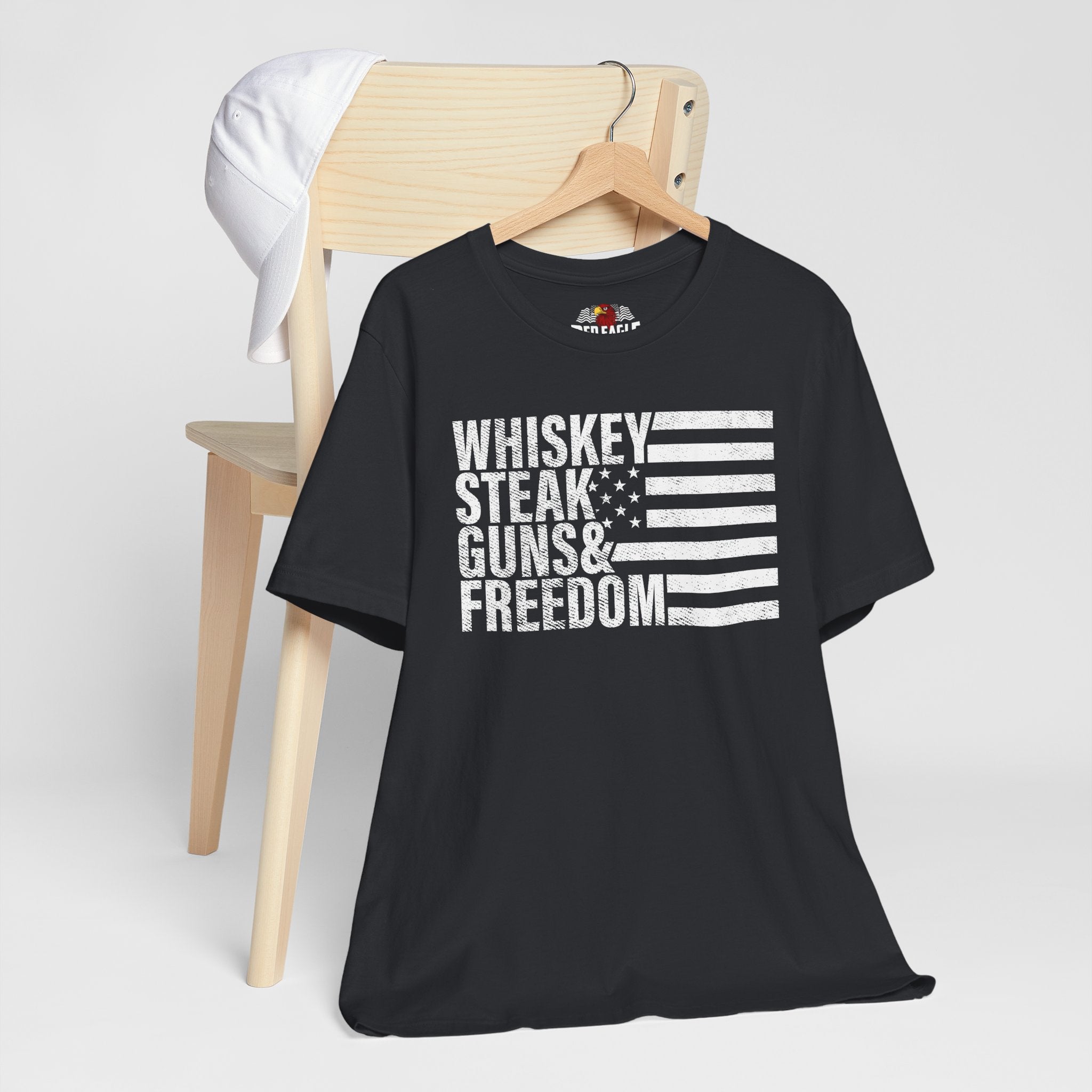 Vintage Black t-shirt with 'Whiskey Steak Guns & Freedom' text and flag design on a wooden chair.